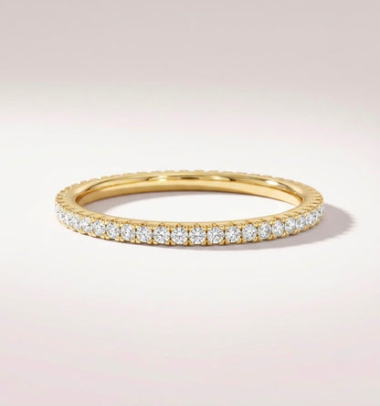 A yellow gold eternity ring set with round brilliant-cut diamonds, shown on a clean, light beige background.